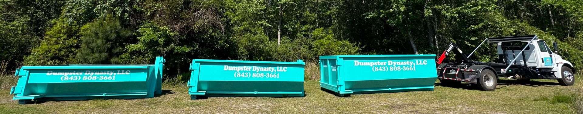 Three turquoise dumpsters aligned beside a black utility truck on a grassy roadside.