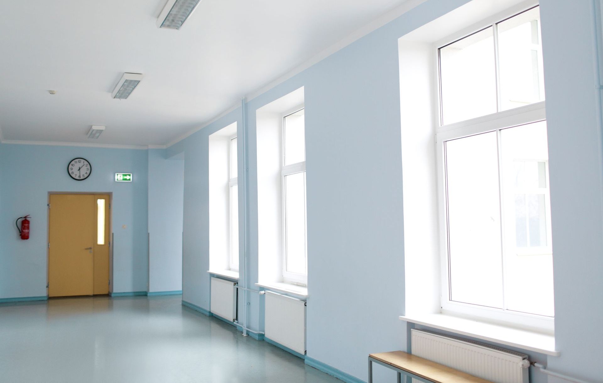 Un couloir vide avec des murs bleus et des fenêtres blanches.