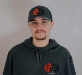 Un homme portant un chapeau et un sweat à capuche se tient devant un mur blanc.