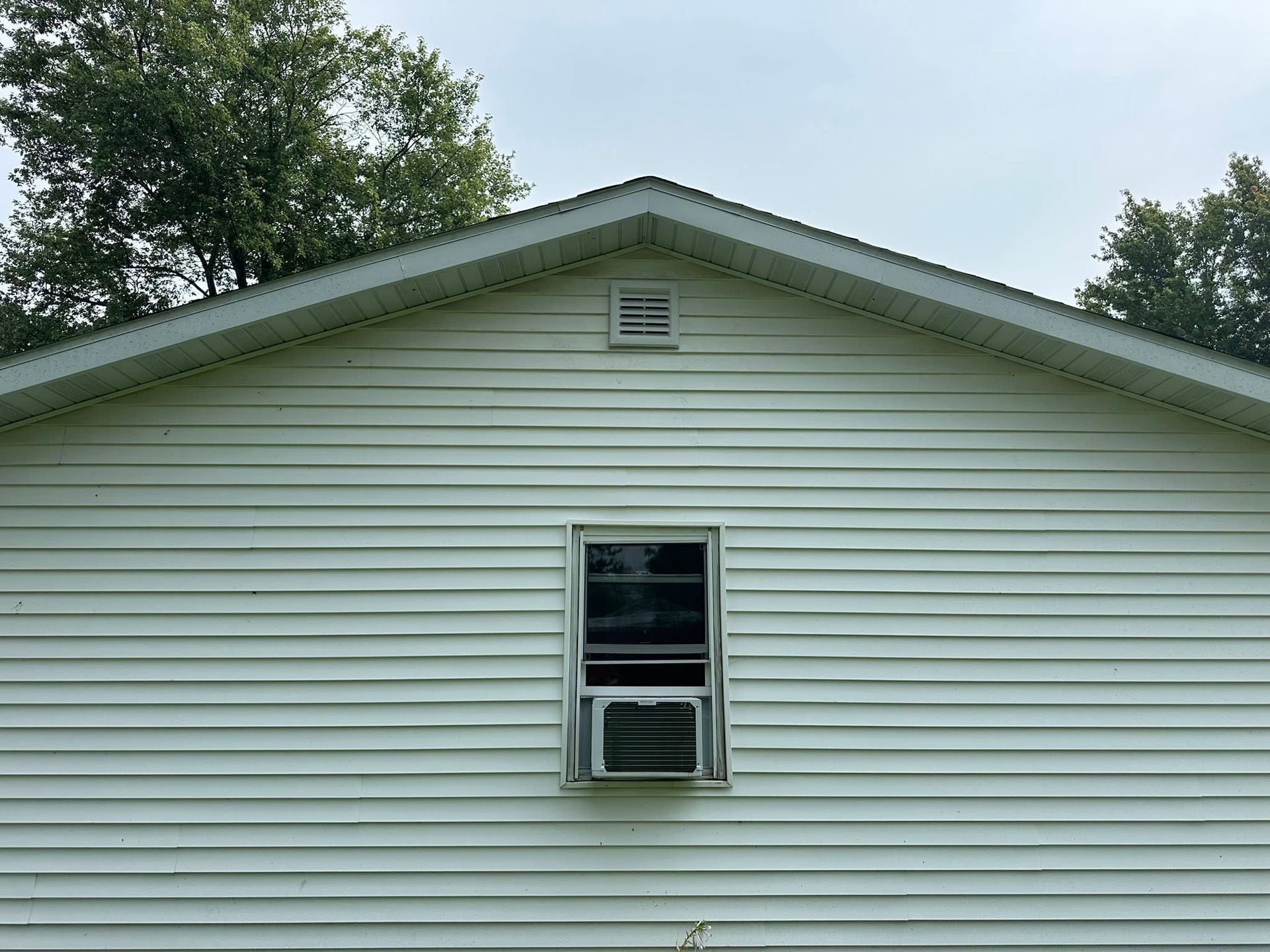 White house siding with a small central window and gable vent under a cloudy sky
