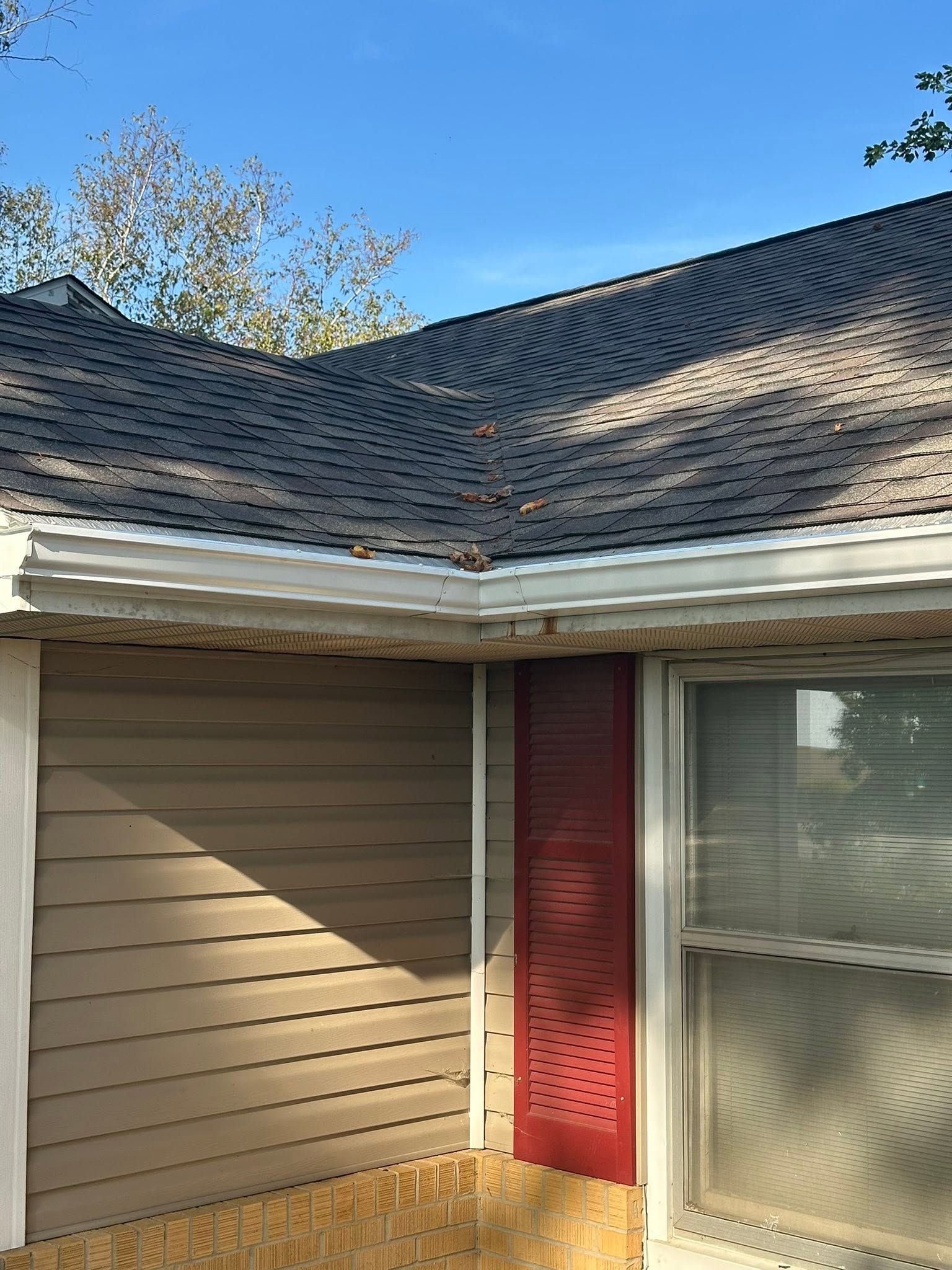 House exterior with tan siding, red shutters, and a dark shingled roof under a blue sky