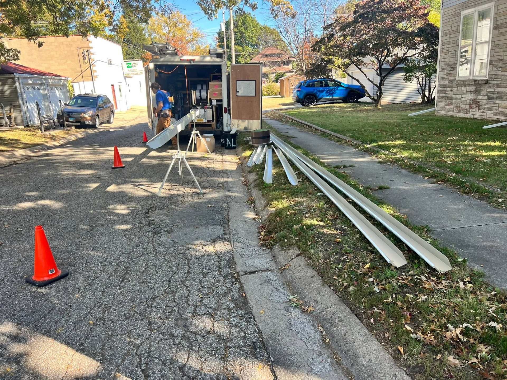 Roadside utility work with cones, tools, and white pipes beside a truck and trailer on a residential street