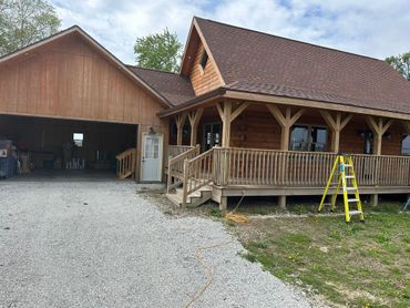 Rustic wooden house with a covered porch, open garage, gravel driveway, and yellow ladder outside