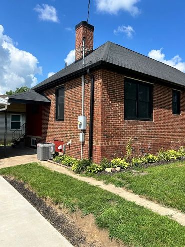 Brick house exterior with black roof, chimney, and small front lawn under a blue sky