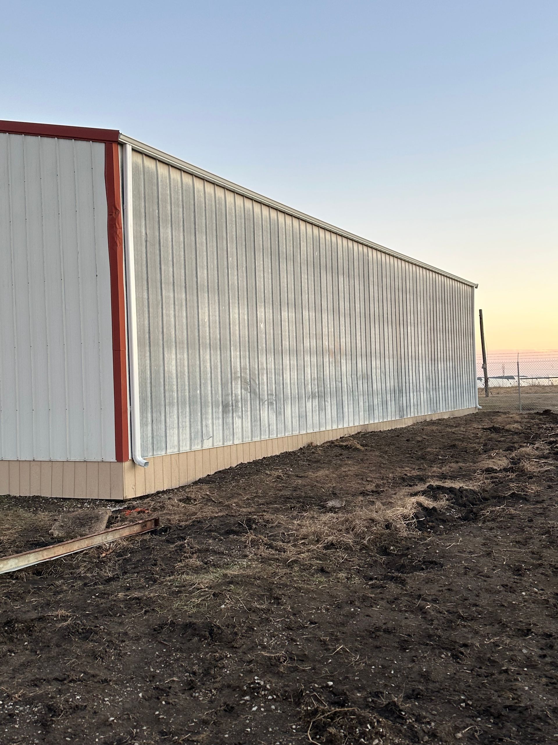 A long white corrugated metal building on a dirt lot at sunset.