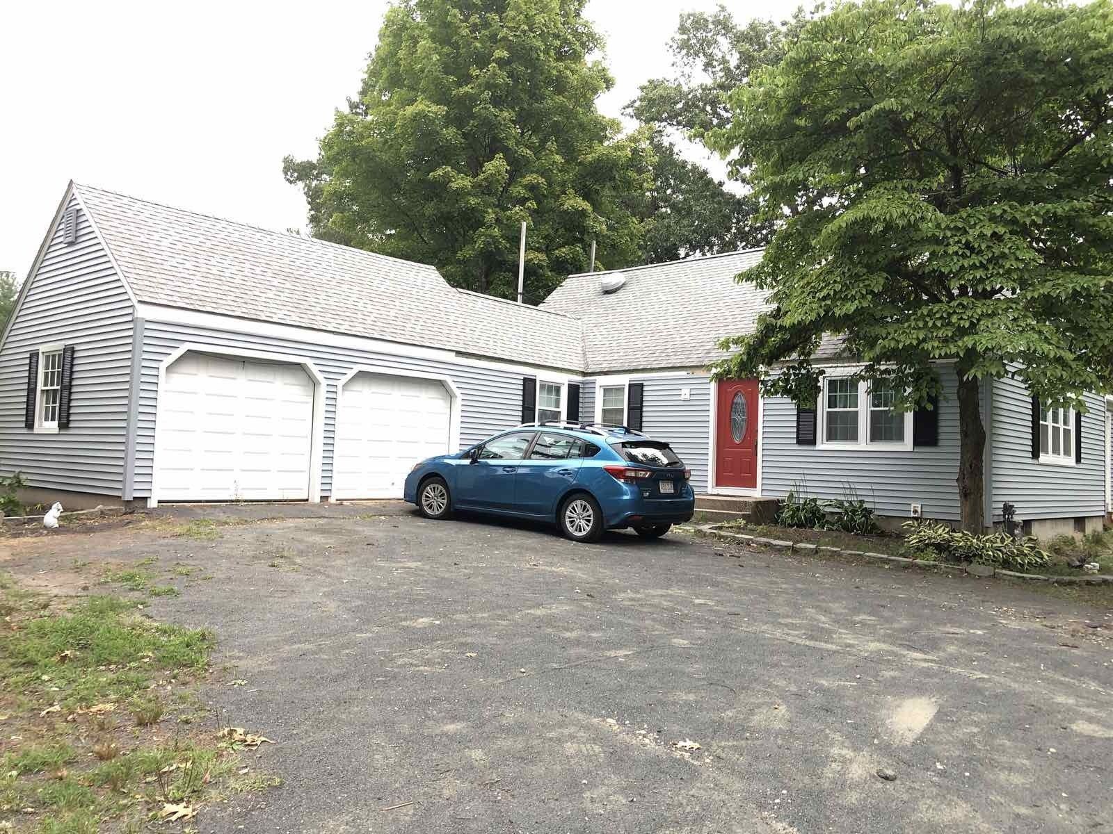 A single-story gray house with a two-car garage, a red front door, and a blue car parked in the driveway.