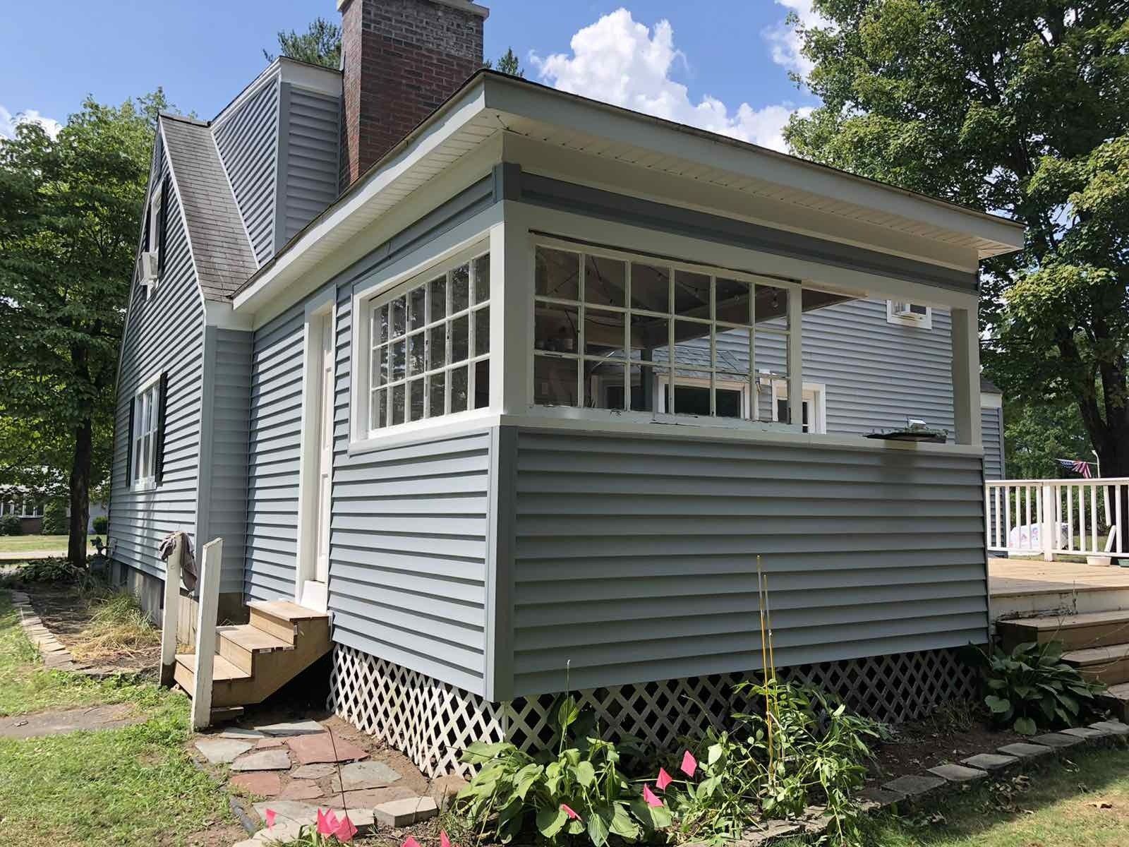 A light blue house with a covered, screened-in porch, white trim, a stone walkway, and lattice skirting on a sunny day.