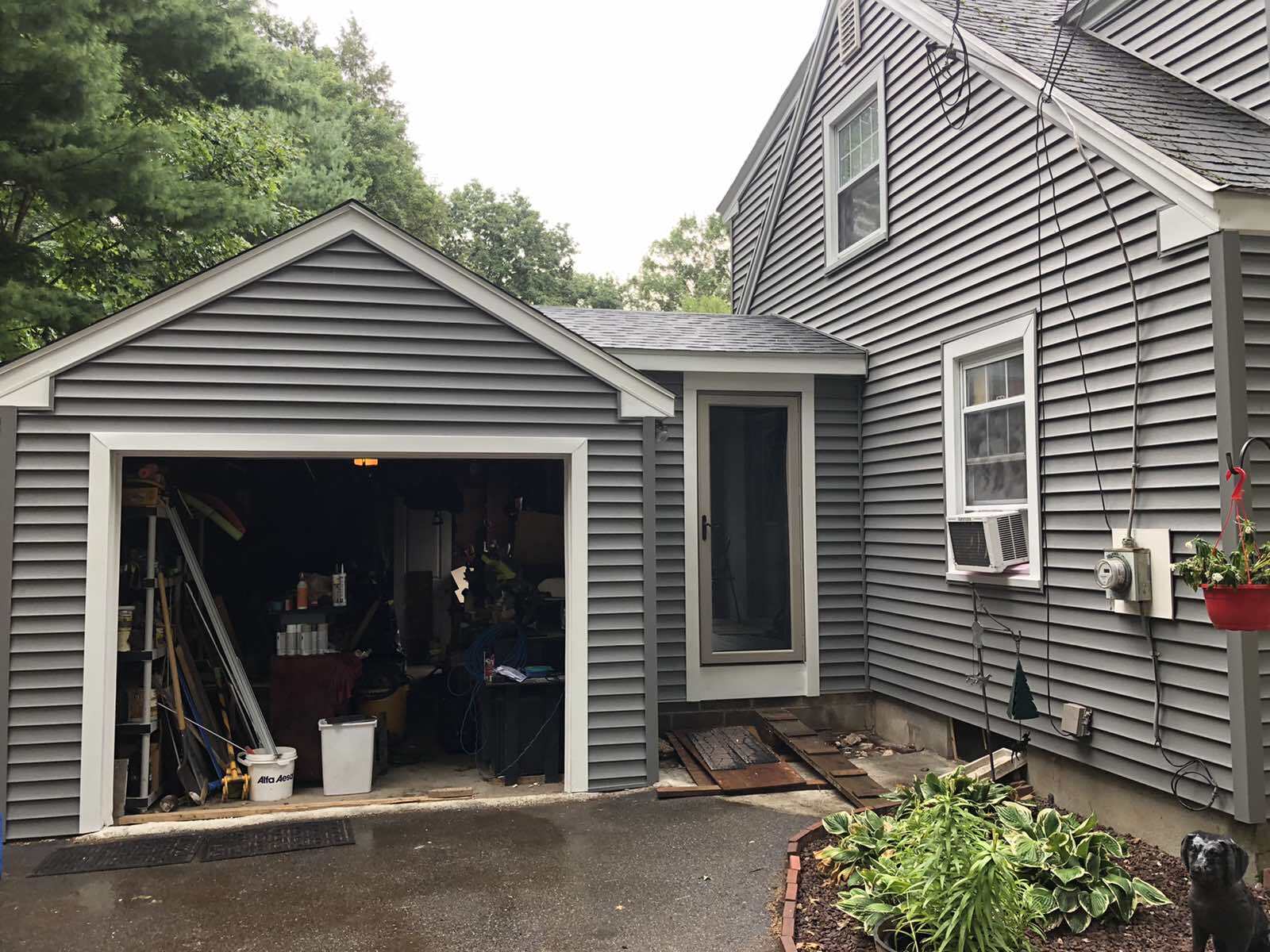 A gray-sided house exterior with an open garage, a side door entrance with a ramp, and a small flower bed in the front.