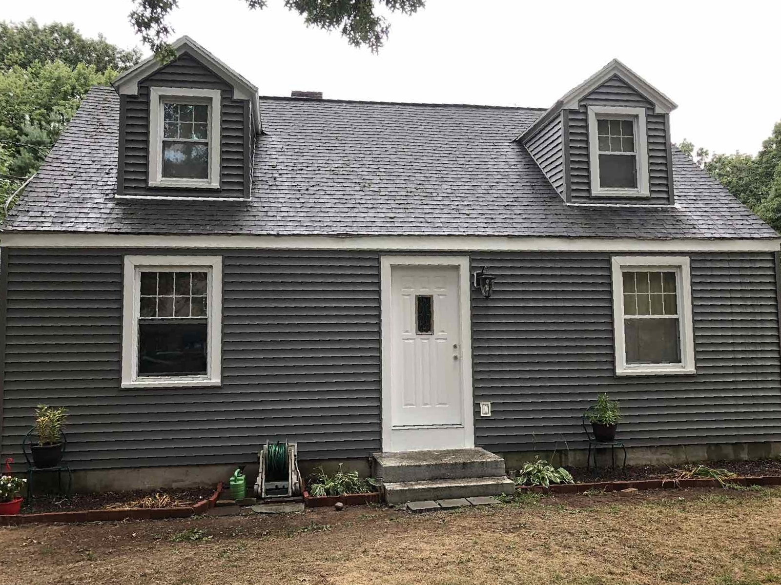 A two-story grey Cape Cod house with white trim, a central white front door, and two dormer windows on the roof.