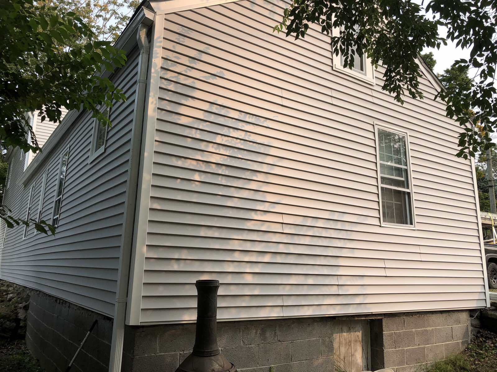 The side of a house with light gray horizontal vinyl siding, a small window, and a dark concrete block foundation.