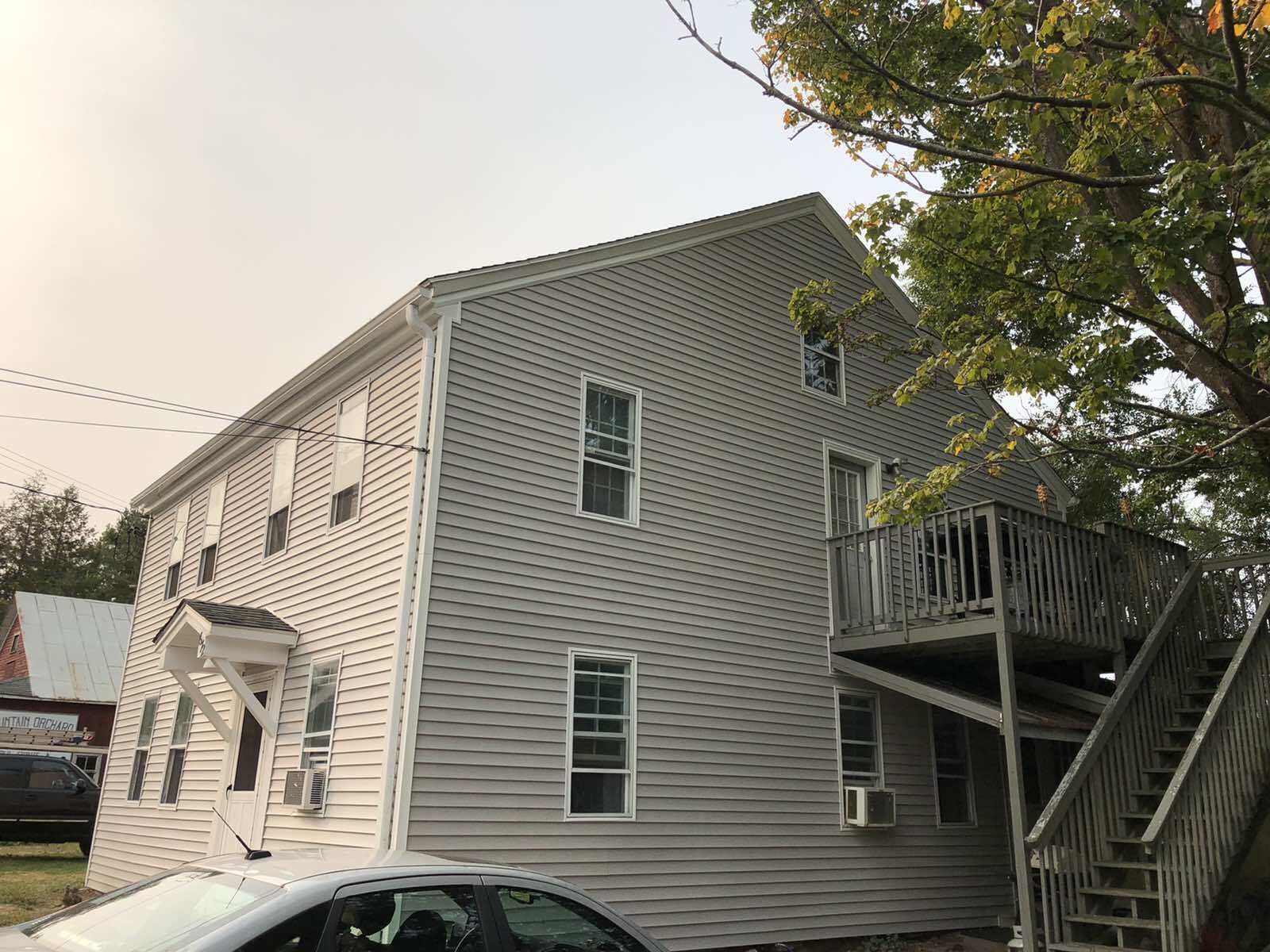 A three-story, light gray siding building with a wooden exterior staircase leading to a second-floor deck.