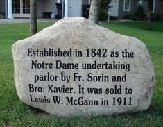 A large rock with a plaque on it that says established in 1842 as the notre dame undertaking parlor