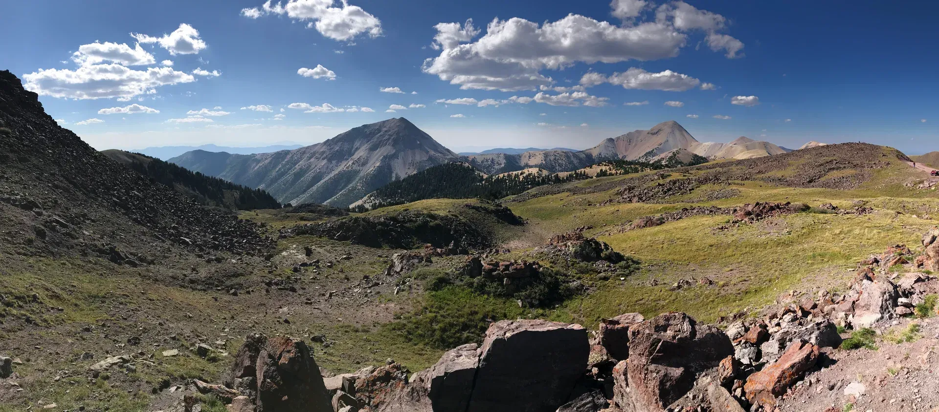 Panoramic view of a rugged, rocky mountain valley under a bright blue sky with scattered clouds.