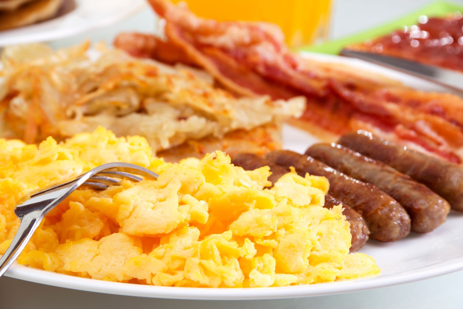 A breakfast plate with fluffy scrambled eggs, crispy bacon, hash browns, and several browned breakfast sausages.