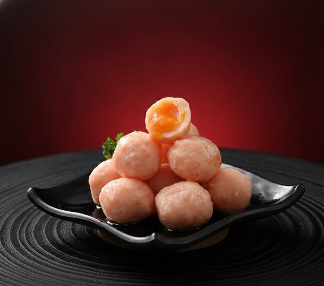 Peach-colored dessert balls stacked on a black plate, with one cut open to show a creamy orange filling.
