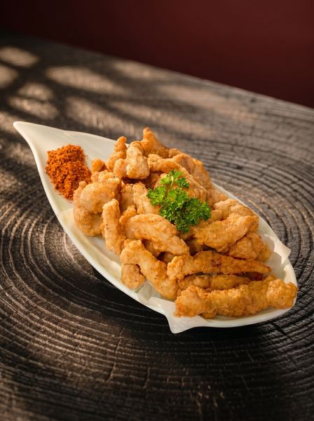 Fried chicken pieces on a white dish, topped with green garnish, on a dark wooden table.