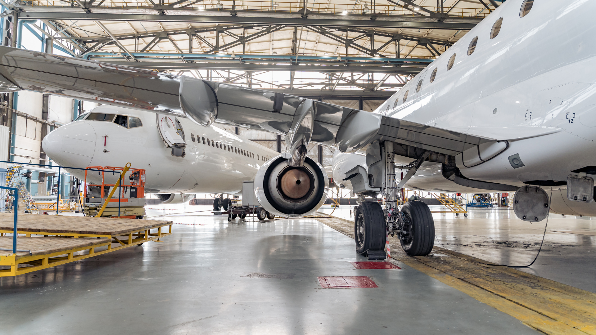 Two white airplanes in a hangar being worked on; visible engines, wings, and landing gear.