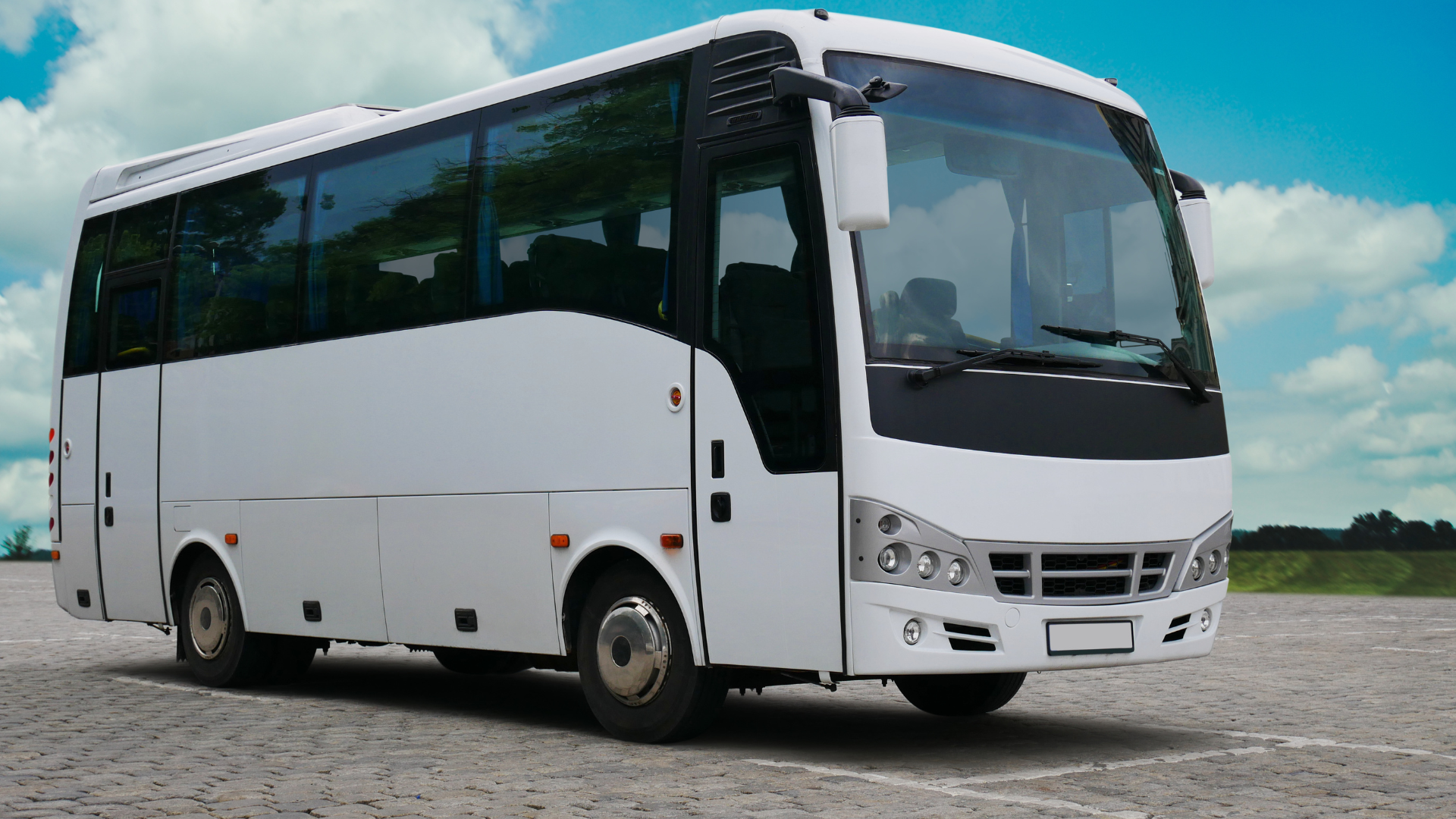 White passenger bus parked on a stone surface under a partly cloudy sky.