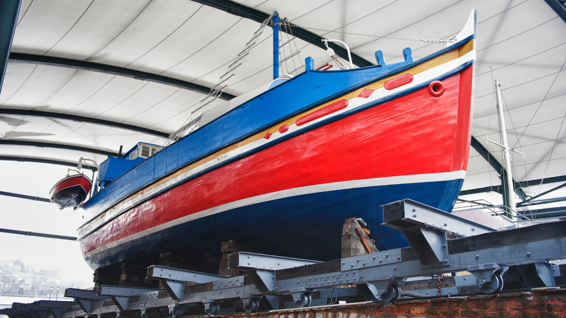 A colorful boat in a shelter, blue hull, red sides, and gold trim, resting on supports.