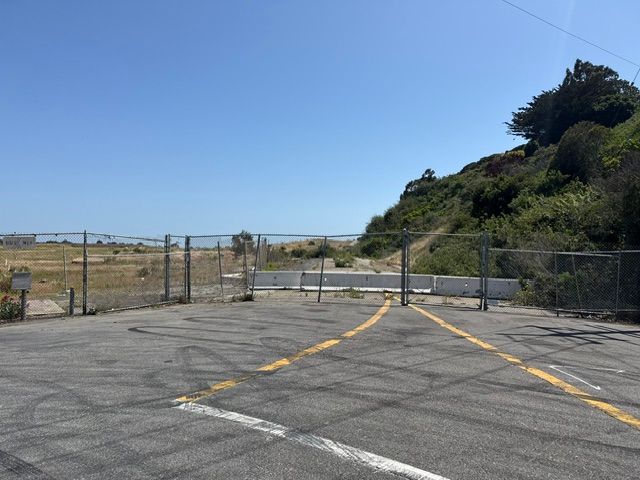 Entrance with gate, leading to a sandy path toward the ocean, under a blue sky.