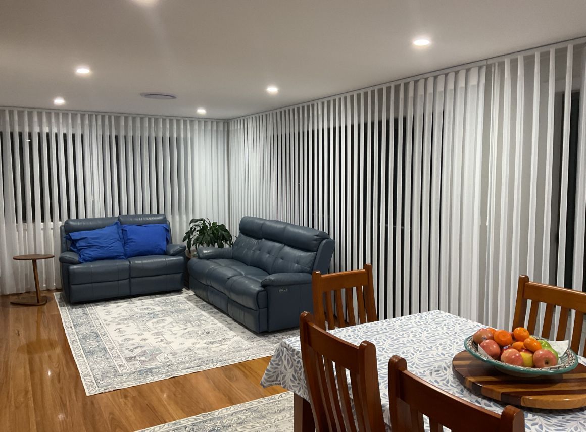 Modern living room with blue sofas, striped curtains, and a dining table with fruit on the right — Port Blinds & Awnings In Laurieton, NSW