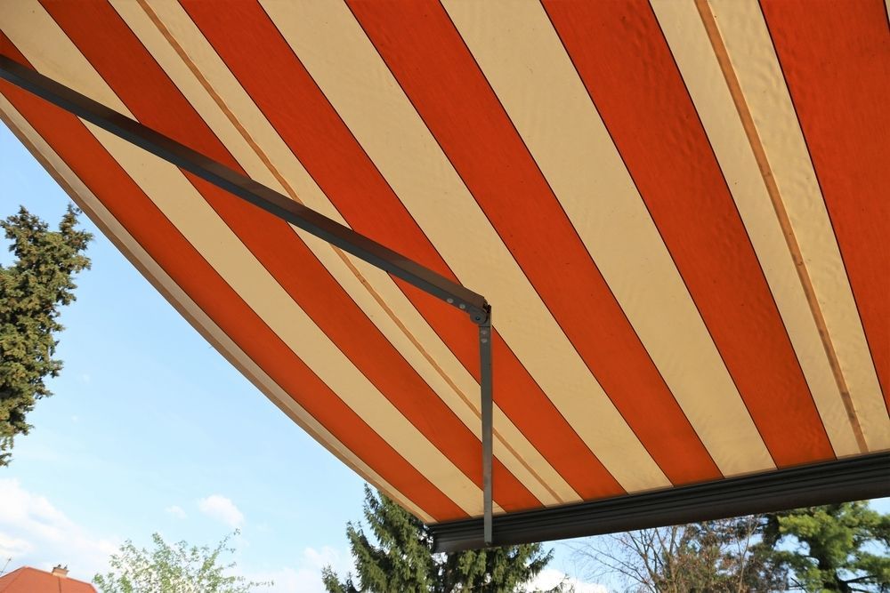 A Red and White Striped Awning With Trees in the Background — Port Blinds & Awnings In Nambucca Heads, NSW
