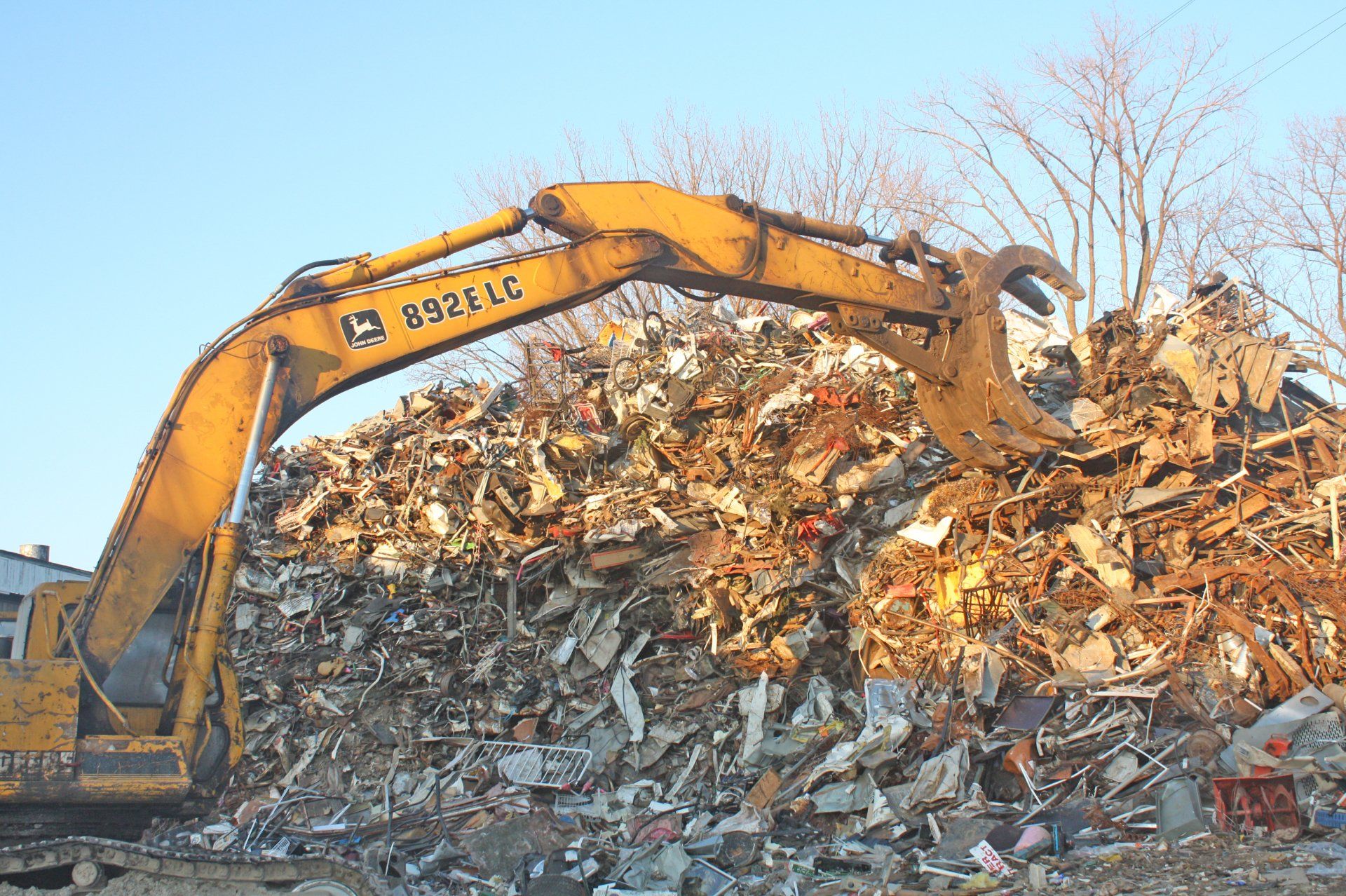 A yellow excavator is working on a pile of scrap metal.