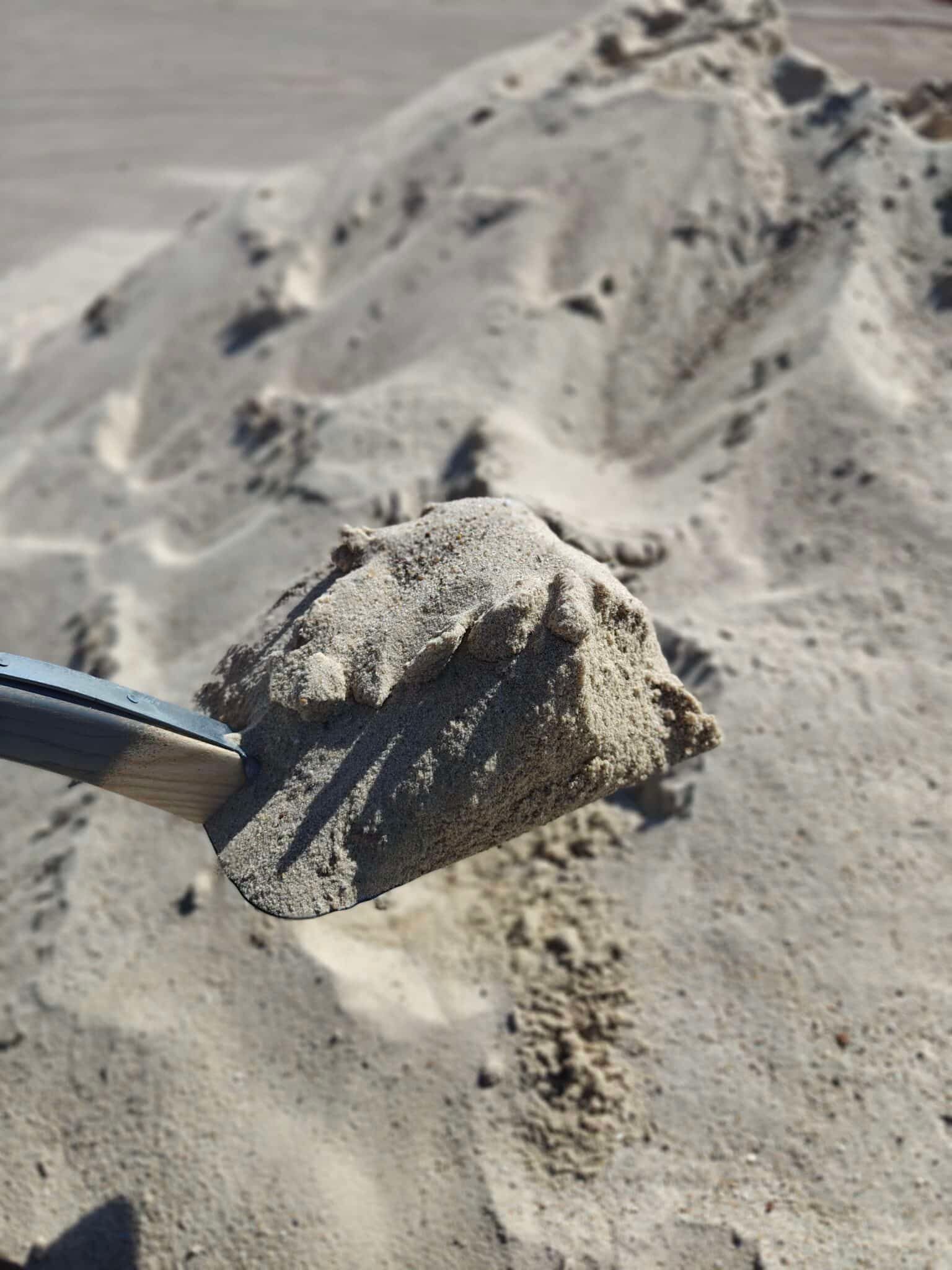 Skovl holder en klump sand mod en sandet bunke baggrund