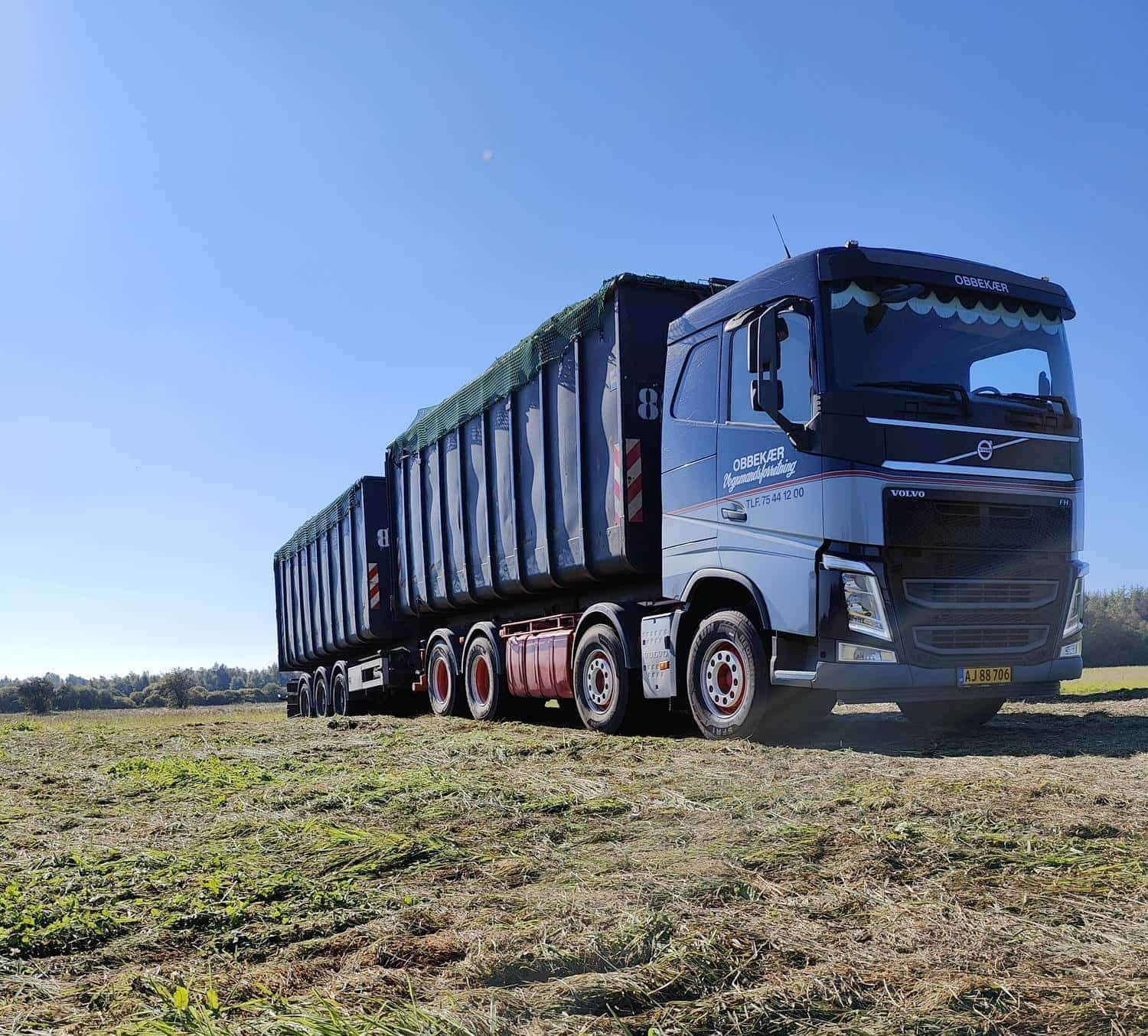 Blå semitrailer, der trækker en lang trailer hen over en græsmark under en klar himmel
