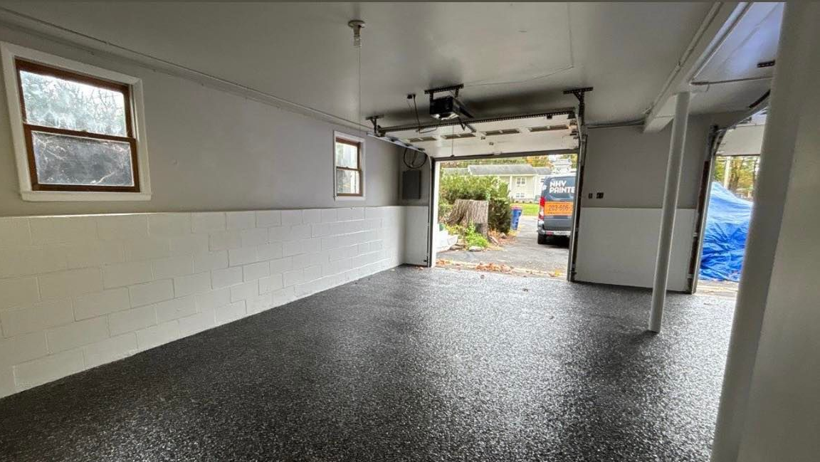 Empty painted garage interior with speckled black floor and open door to driveway outside