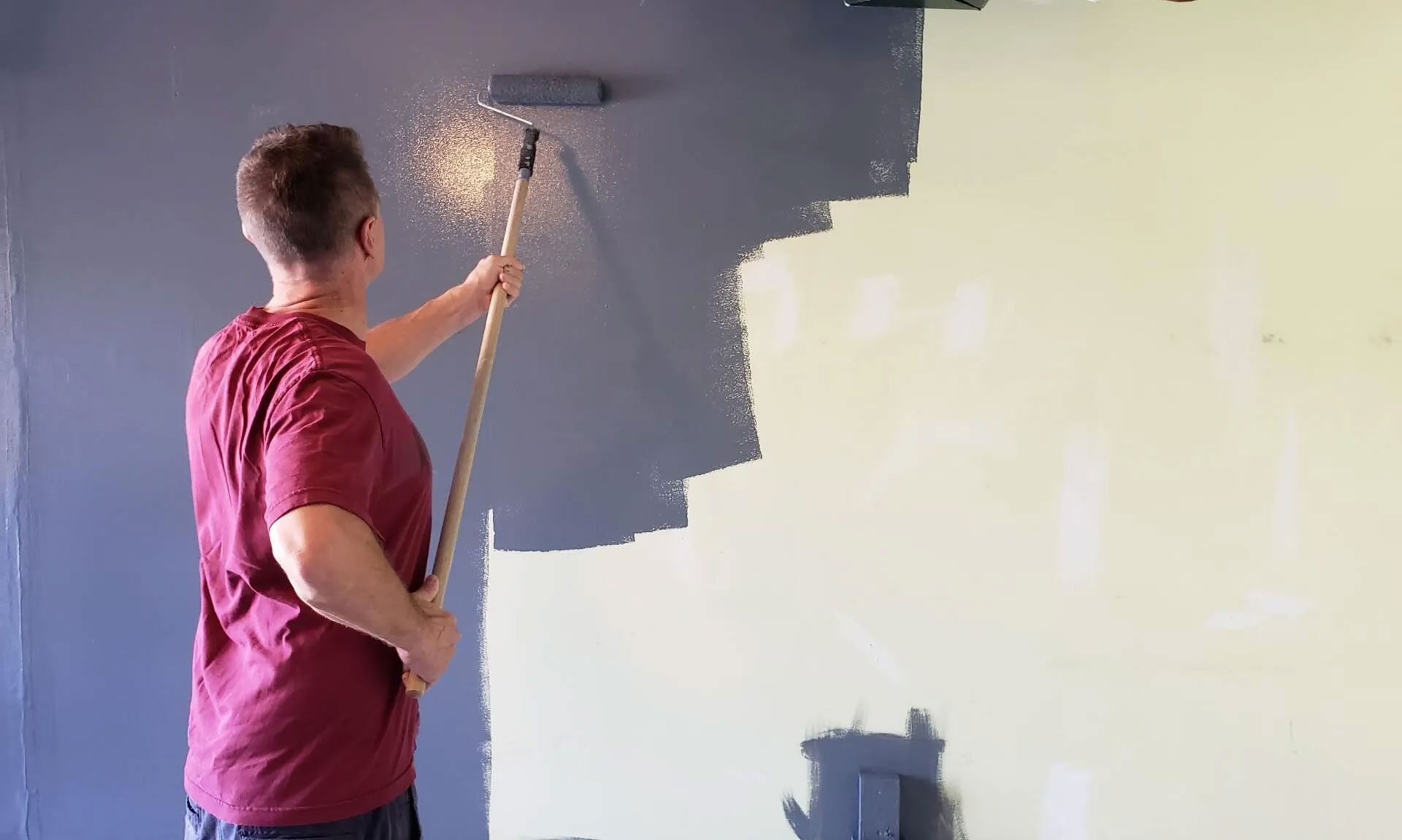 Person painting a wall blue with a roller on a pole.