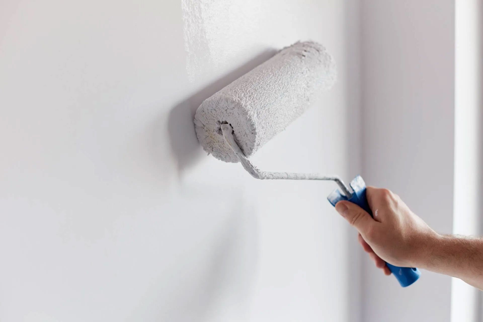 Person painting a white wall with a paint roller.