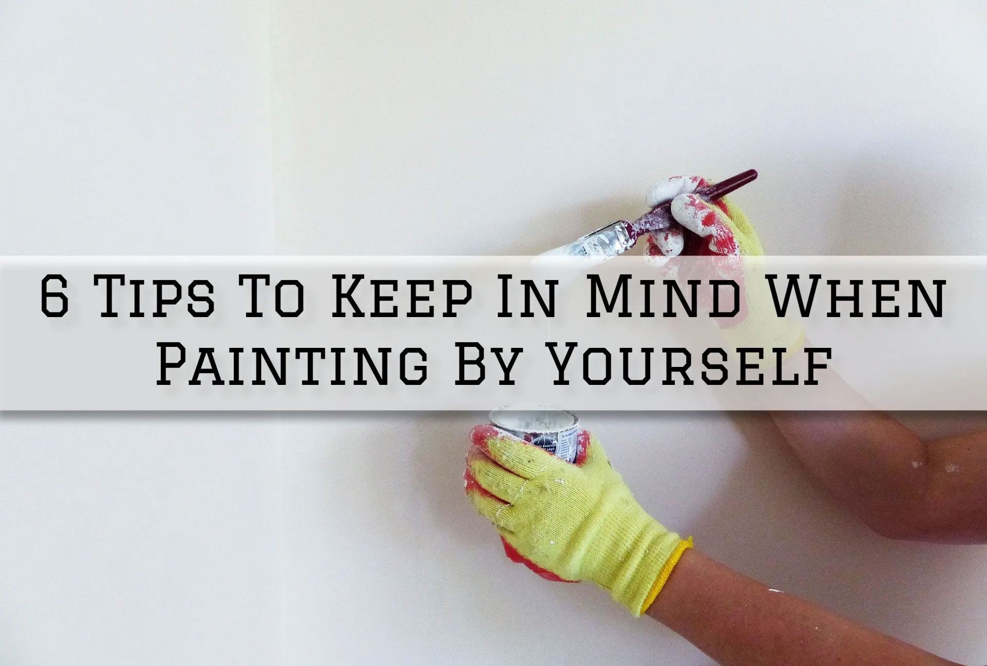 Person painting a white wall wearing yellow gloves. Text overlay: