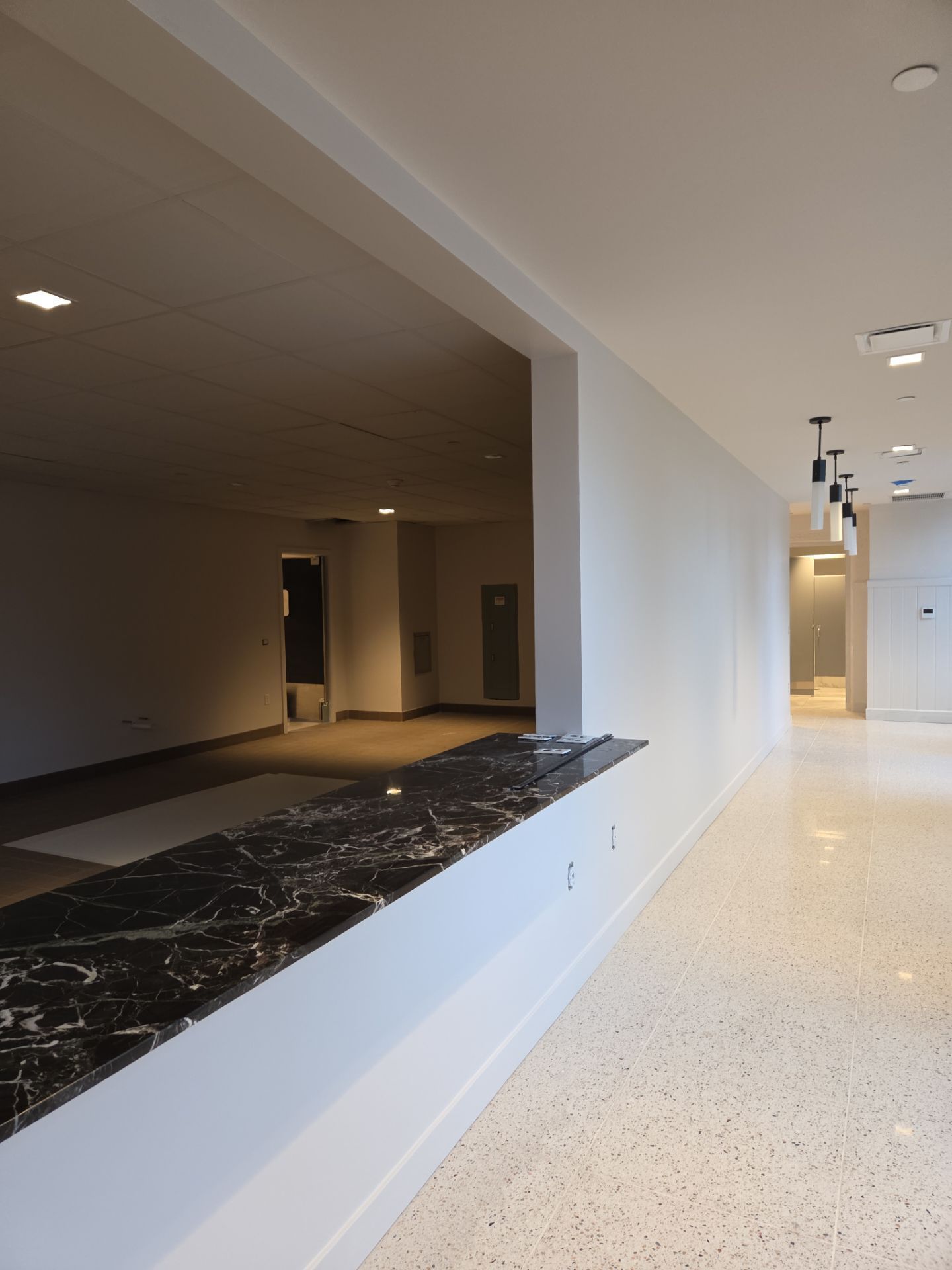Interior view of a building with a black marble counter, open doorway, and a long hallway with lights.
