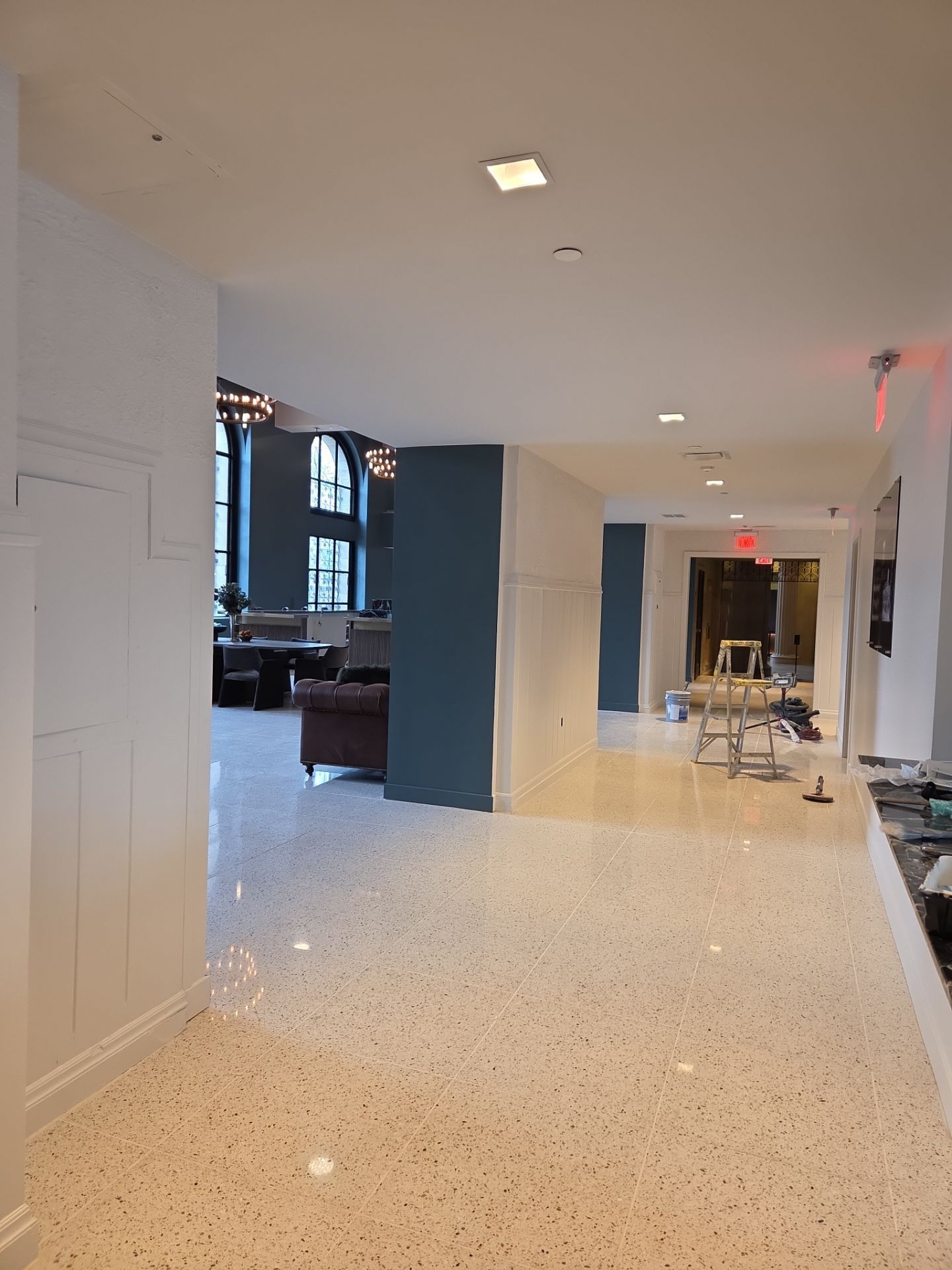 Hallway with terrazzo floor, white and blue walls, and a view into a lounge area.