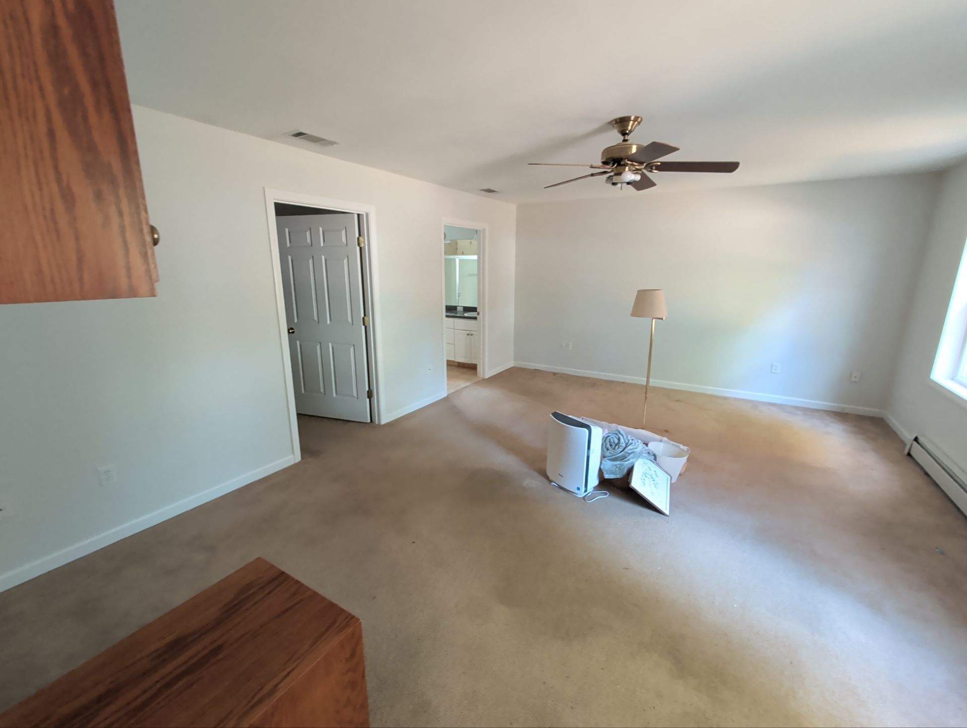 Empty living room with tan carpet, white walls, and a ceiling fan. A door leads to another room.