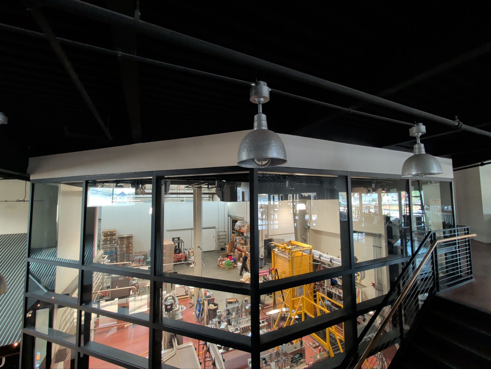 Glass-walled observation room overlooking a machinery-filled factory floor, with overhead lights and a black ceiling.