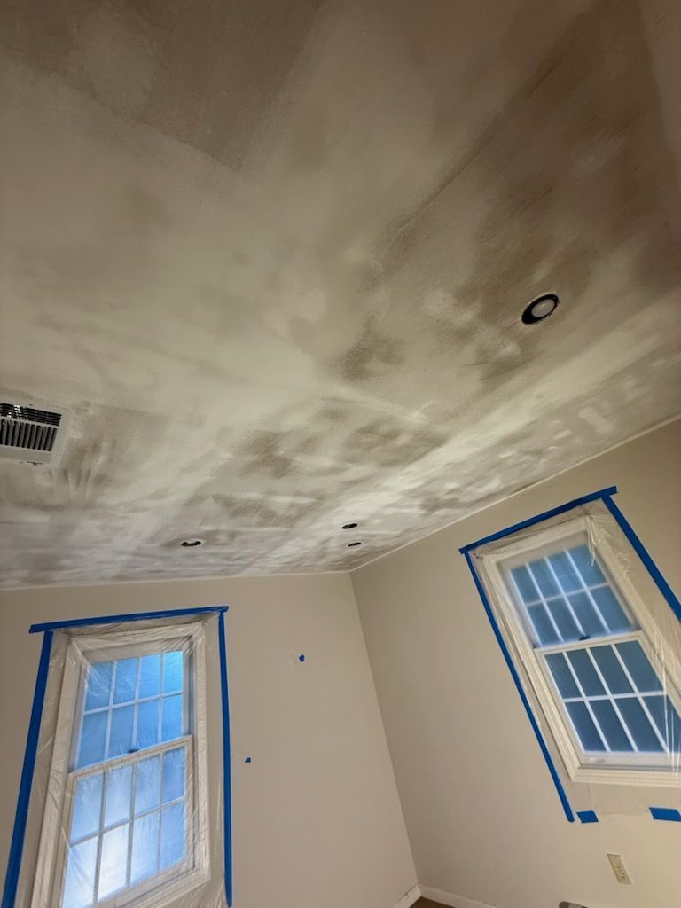 Room interior with recently plastered ceiling and two taped-off windows.