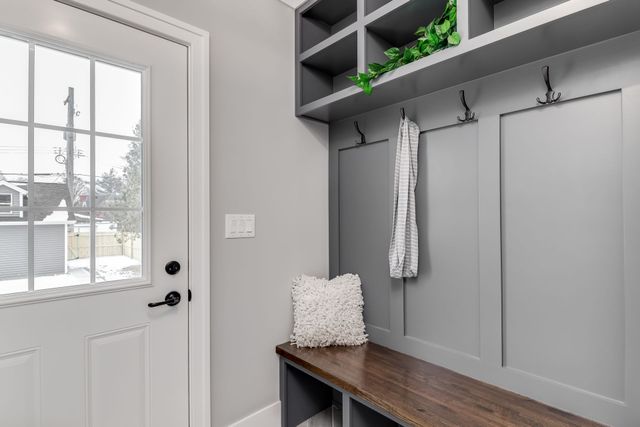 Entryway with white door, gray mudroom bench, hooks, and cubbies beside a window.