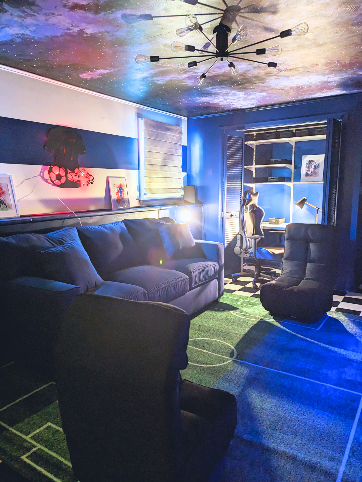 Cozy blue gaming room with galaxy ceiling, sofa, armchairs, desk, and green & blue floor.