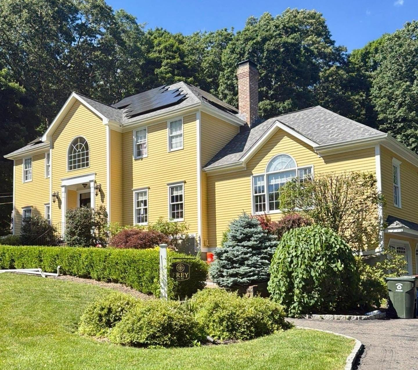 Yellow two-story house with white trim, solar panels, and landscaped lawn on a sunny day