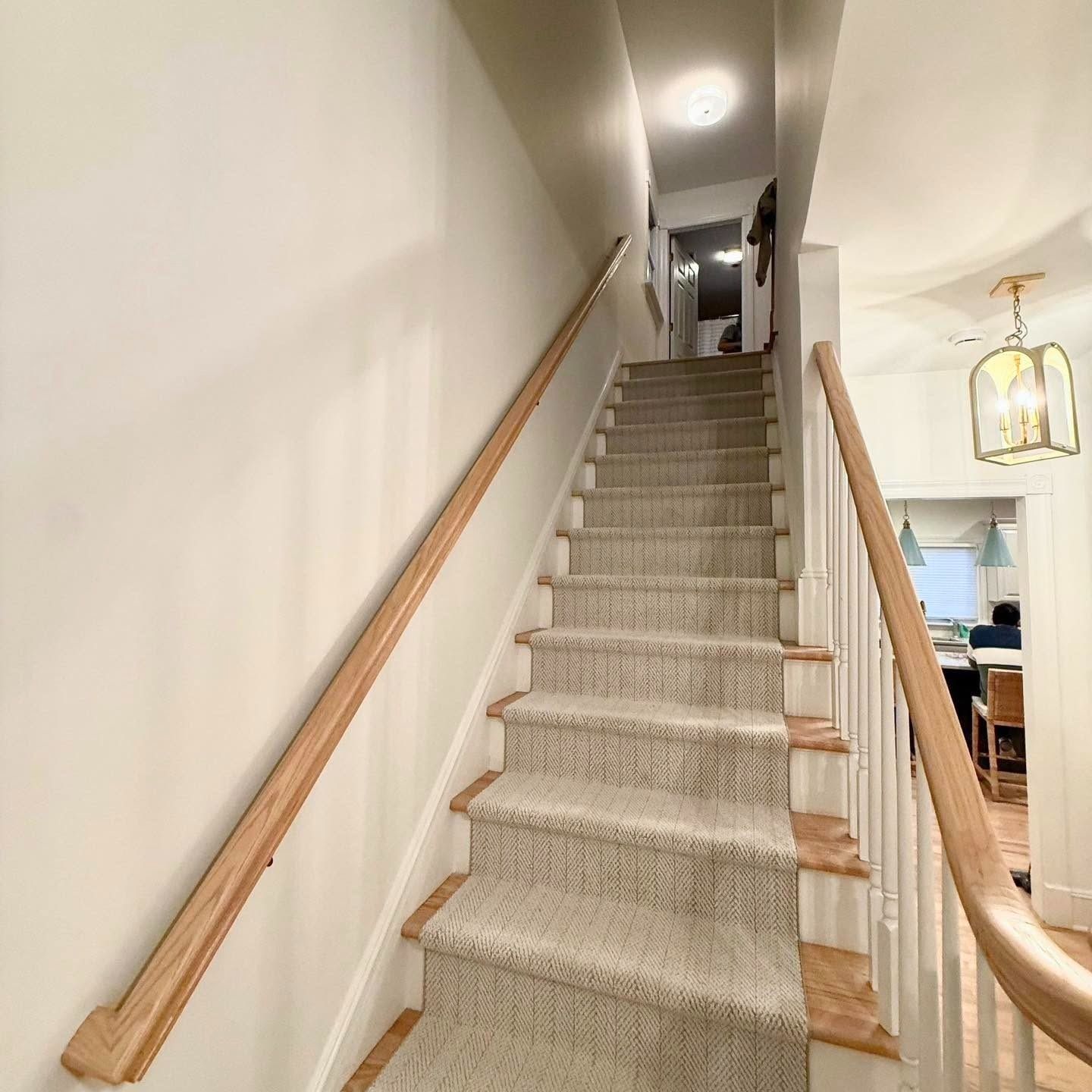 Indoor staircase with beige carpet, wooden handrails, and hallway view at the top