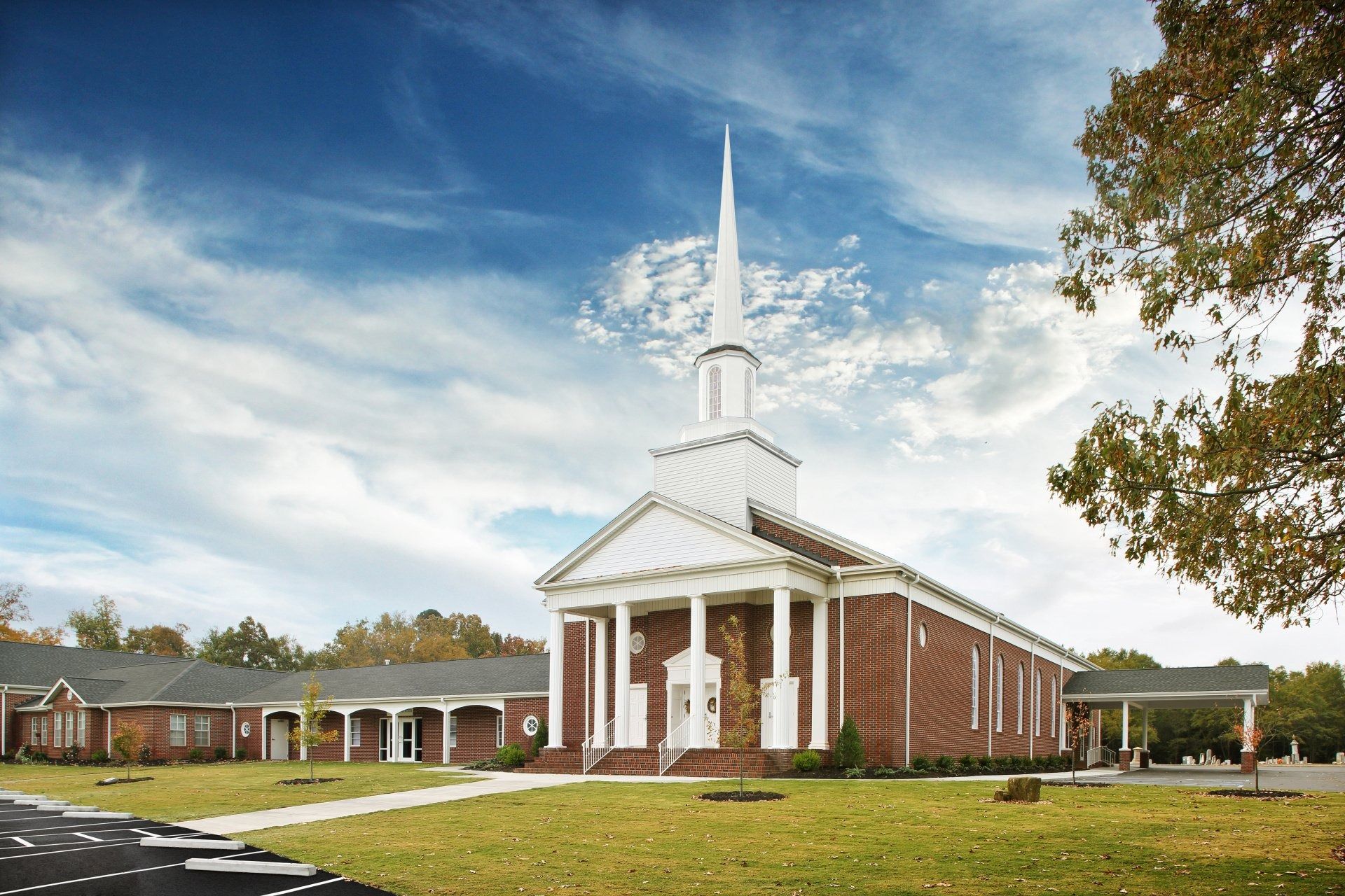 Brick church building with white steeple, columns, and a blue sky with clouds.