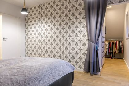 Bedroom with floral wallpaper, a bed, and a closet partially concealed by curtains. Light wooden floors and a hanging light are visible.