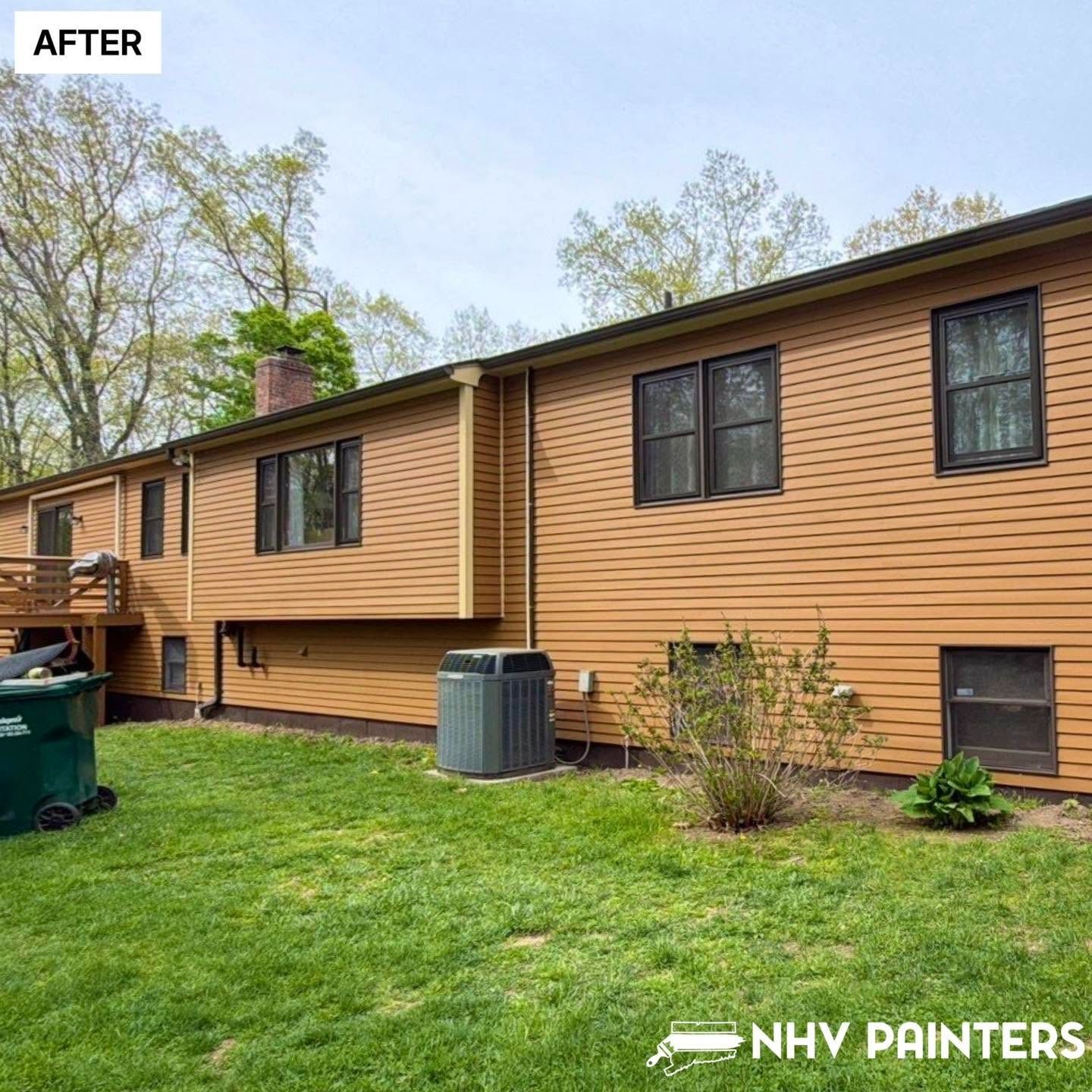 Brown-sided house exterior with black-trimmed windows, green lawn, and HVAC unit after painting.