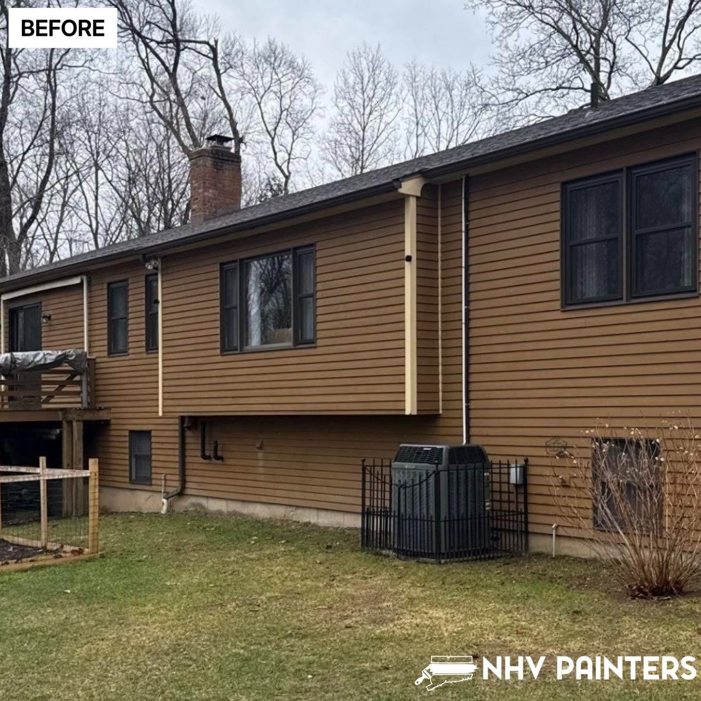 Before view of a brown-sided house with a deck, windows, chimney, and lawn.