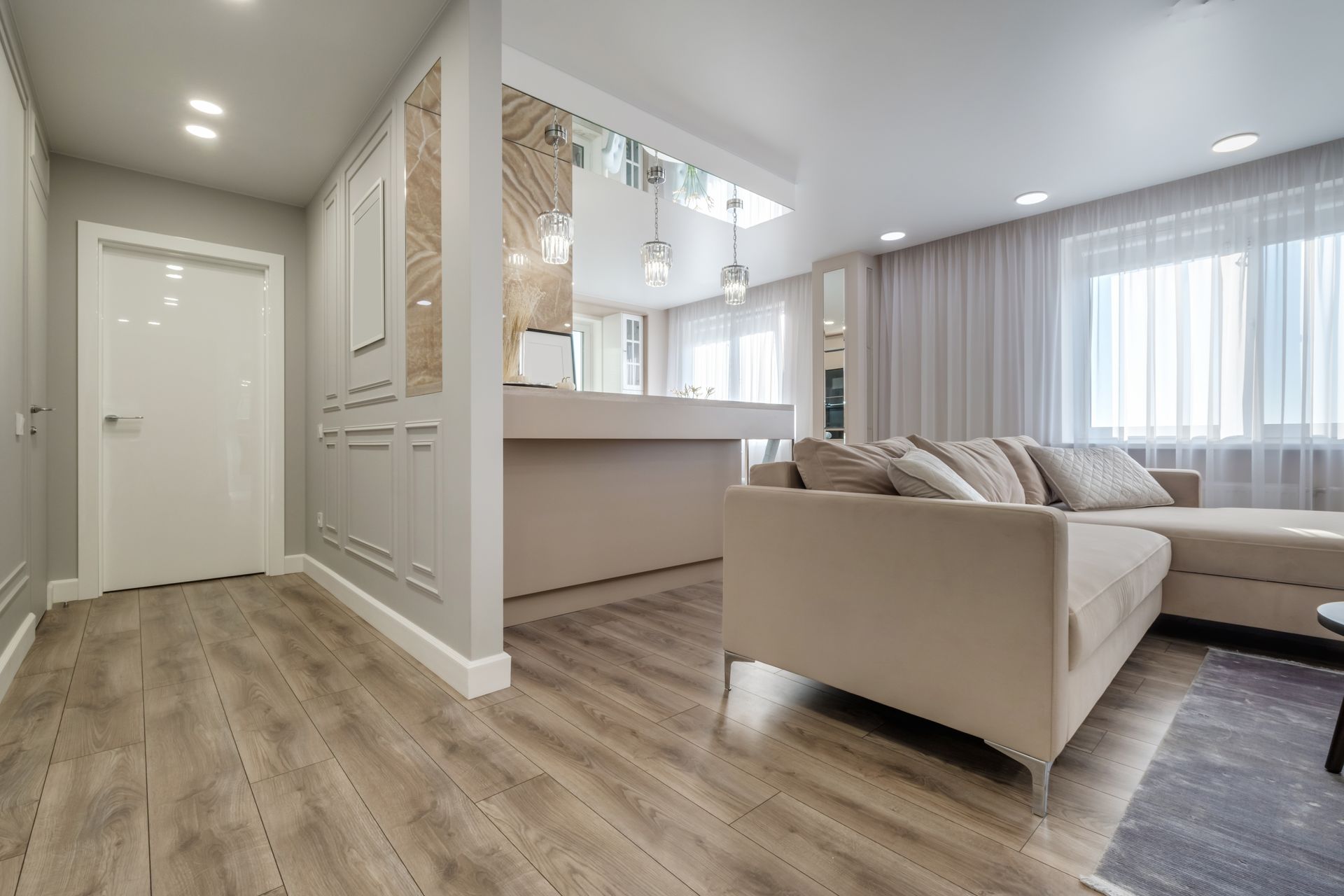Modern open-concept hallway and living room with luxury vinyl plank floors, beige sofa, and bright windows.