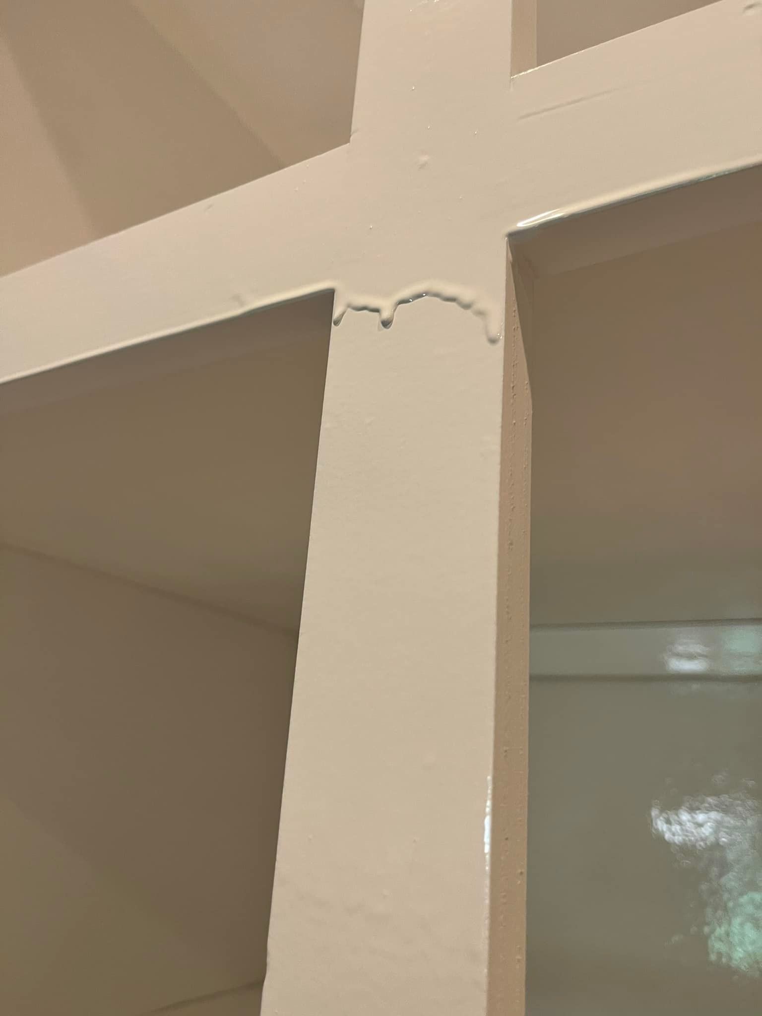 Close-up of a white painted wall with a cross-shaped structure. Some paint dripped at the intersection.
