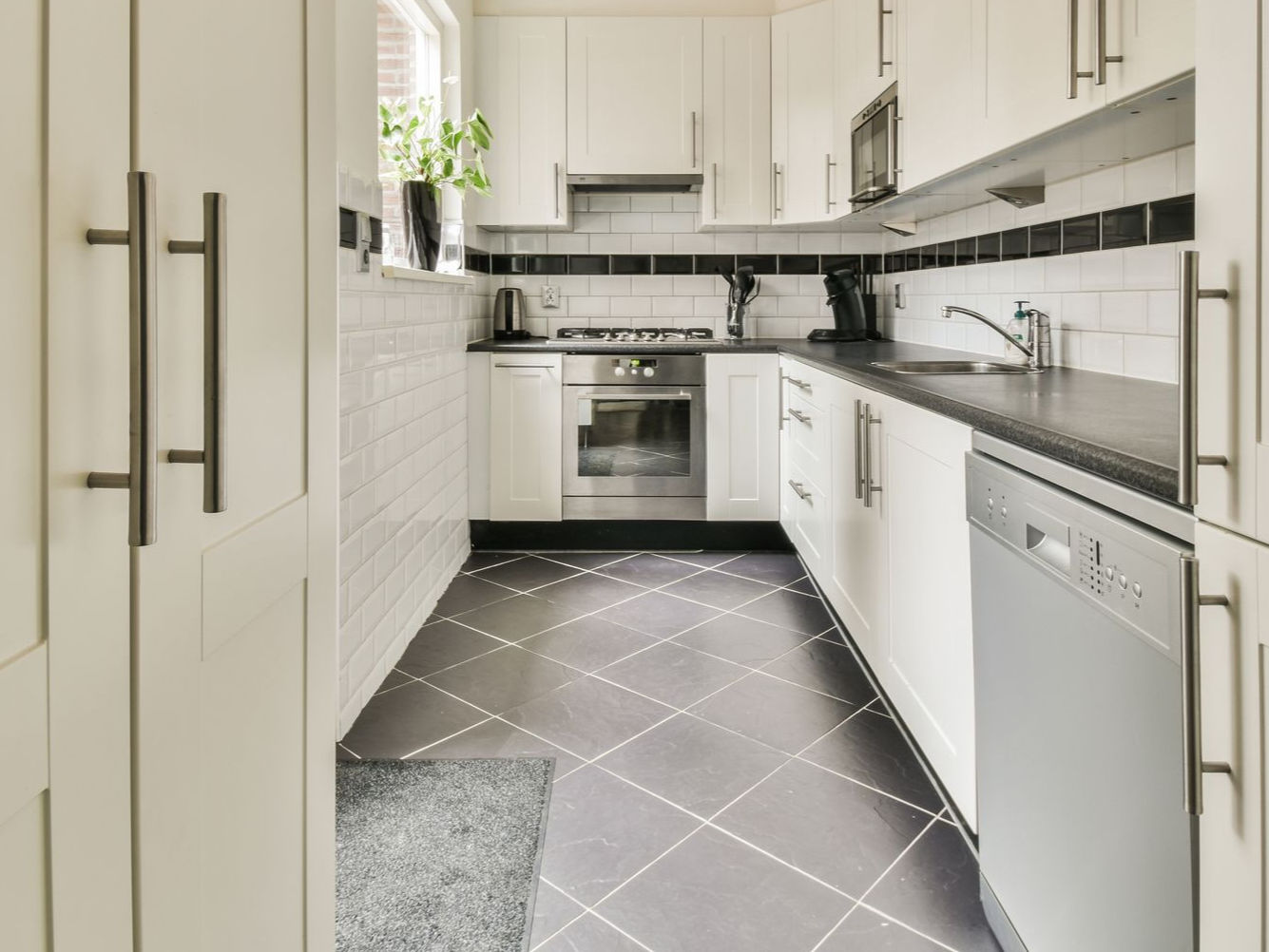 Bright white galley kitchen with black tile floor, stainless appliances, and long cabinet handles