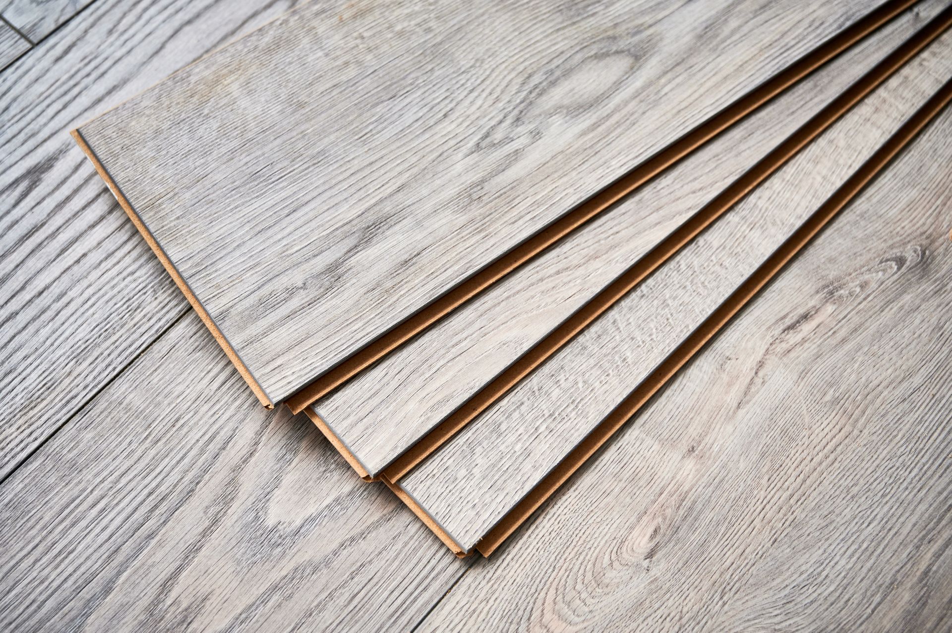 Stacked light wood laminate planks on a gray wood floor.